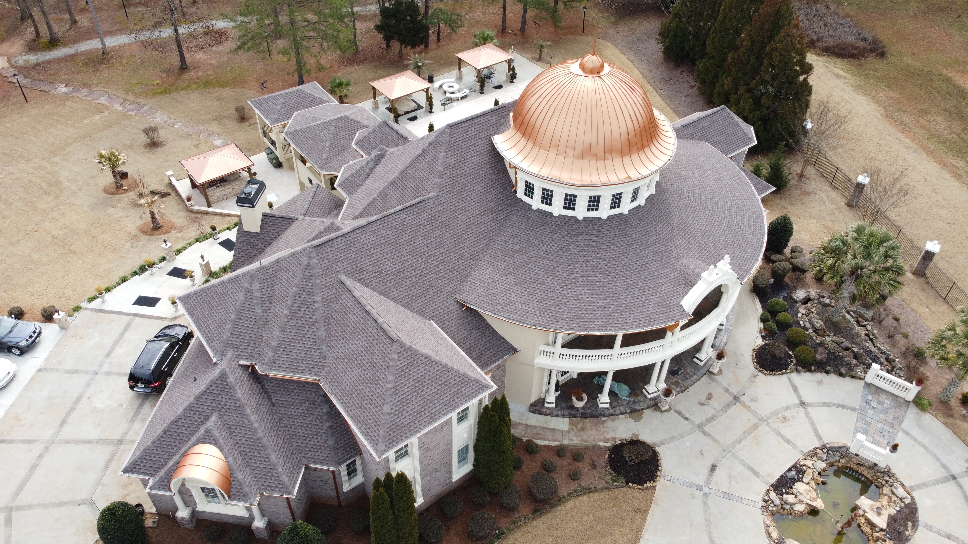 Aerial drone view of luxury mansion with copper dome and complex roof architecture by 1 Source Roofing